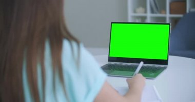 Laptop bilgisayarı Green Mockup Screen 'den not alan bir kız. Bilgisayarda öğrenen kız
