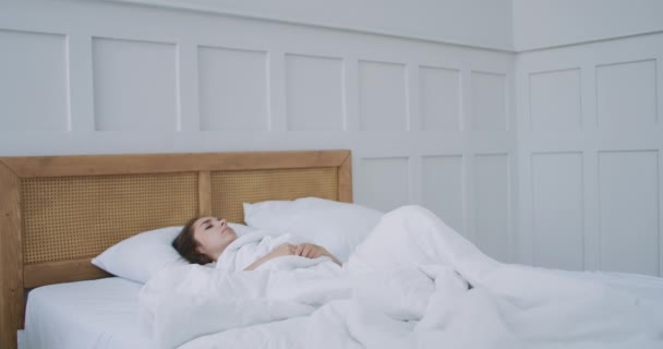 Jonge vrouw wordt wakker in bed in de ochtend glimlachend steekt haar handen op — Stockvideo