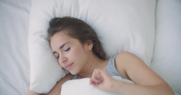 Jonge vrouw wordt wakker in bed in de ochtend glimlachend steekt haar handen op — Stockvideo