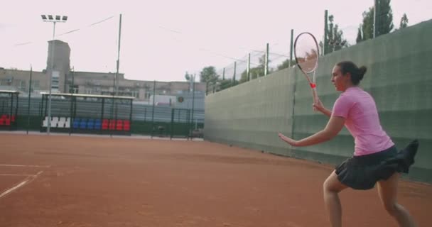 Joven mujer caucásica jugando al tenis en una cancha, devolviendo una pelota en cámara lenta — Vídeo de stock