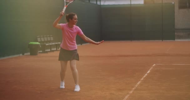 Genç bir kadın tenis kortunda raketle yürüyor. Mavi gömlekli ve siyah şortlu çekici esmer kadın tenis kortuna giriyor. Kopyalama alanı ile tam uzunluk takip çekimi — Stok video