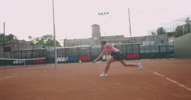 Sahada tenis oynayan, ağır çekimde topu geri getiren beyaz bir kadının yan görüntüsü.