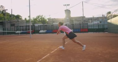 Genç bir kadın tenis kortunda raketle yürüyor. Mavi gömlekli ve siyah şortlu çekici esmer kadın tenis kortuna giriyor. Kopyalama alanı ile tam uzunluk takip çekimi