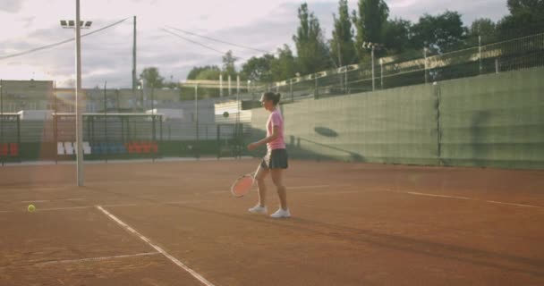 Atleta atractivo posa cerca de la red en la cancha de tenis. Joven atlética jugando al tenis, caminando en una cancha cubierta, jugadora en una posición de juego, día de entrenamiento — Vídeo de stock