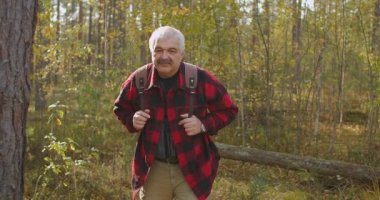 Orta yaşlı gezgin sonbahar günü güneşli bir havada ormanda yürüyor, sırt çantası taşıyor, doğanın ve sessizliğin tadını çıkarıyor.