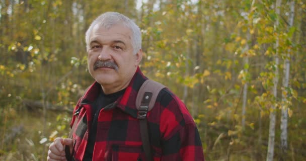 Ritratto di turista dai capelli grigi con i baffi nella foresta durante la giornata autunnale, l'uomo sorride alla macchina fotografica, ecoturismo — Video Stock