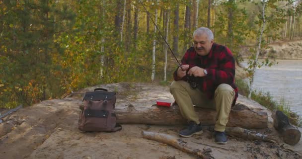 Veselý muž středního věku se připravuje na rybaření na pobřeží lesní řeky, na ekologicky čistém místě, relaxaci a hobby — Stock video