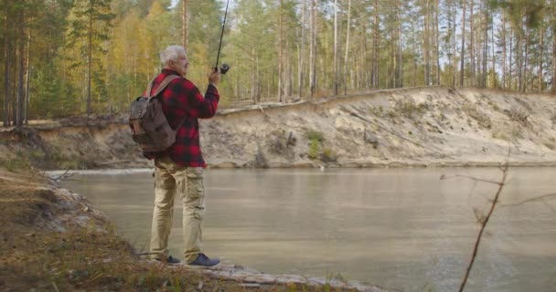 Pesca na costa do reservatório, o homem está lançando haste de pesca na água, descanso e viagens na natureza, descanso solitário no fim de semana — Vídeo de Stock