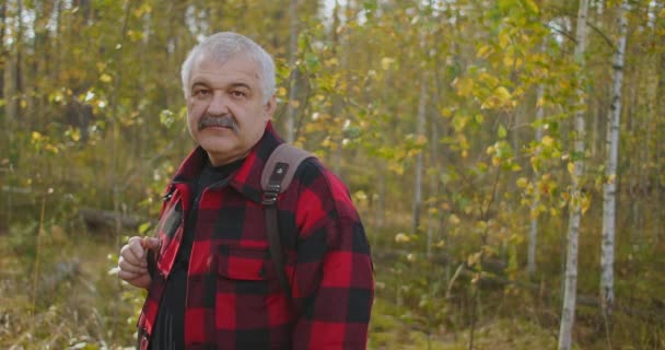 Pozytywny turysta w średnim wieku z plecakiem uśmiecha się i patrzy w obiektyw, portret mężczyzny w lesie jesienią podczas wędrówki — Wideo stockowe