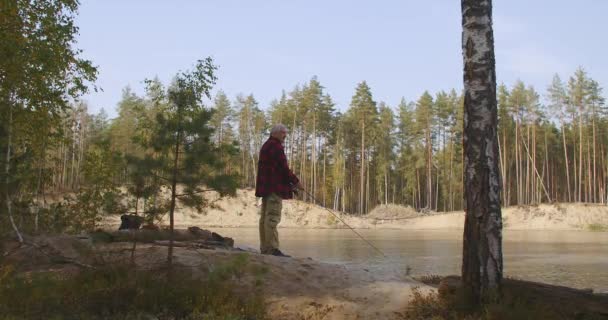 Homem solitário está pescando na costa do rio na floresta na manhã ensolarada, descansando em férias, de pé com vara na mão — Vídeo de Stock