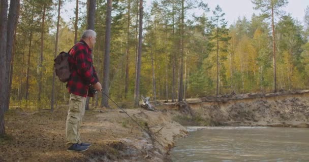Homem adulto está pescando peixe no lago na floresta, usando haste de pesca de giro, de pé na costa na floresta, caminhante está pescando — Vídeo de Stock