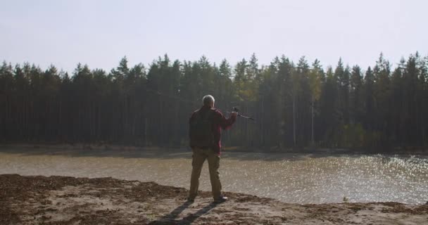 Hombre inspirado en la orilla alta del río está disfrutando y admirando la naturaleza, vista trasera de la figura masculina, pescador con caña — Vídeo de stock