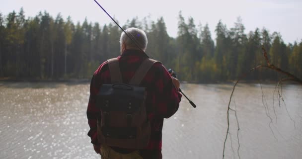 Pescador está viendo el lago en el bosque, elegir el lugar para la pesca y disfrutar de la naturaleza en la temporada de otoño, vista posterior de la persona — Vídeo de stock