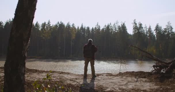 Pescador es inspirador por la naturaleza, ver en el río o lago en la temporada de otoño, vista trasera del hombre de mediana edad en el acantilado — Vídeo de stock