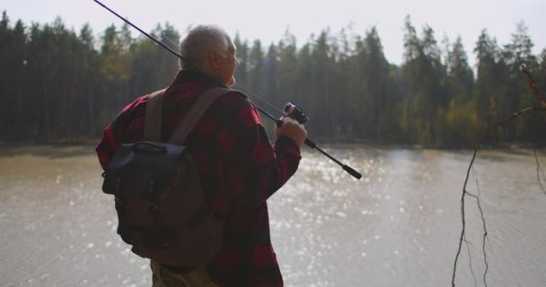 Resenär med ryggsäck och fiskespö står på hög kust av floden och beundrar naturen — Stockvideo