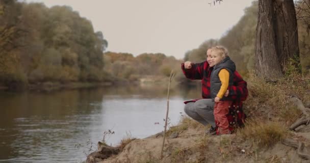 Щасливі сімейні вихідні восени, жінка з маленькою дитиною насолоджується лісовим ландшафтом з озером, мати виховує маленького сина — стокове відео