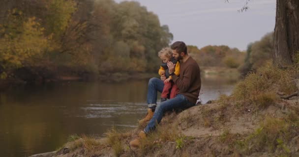 Familjen helg i naturen, mannen och hans son sitter på stranden av sjön och avkopplande, andas frisk luft — Stockvideo