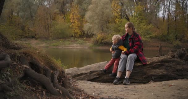Tidig nedgång i skogen, människor går vid bra väder, mor och barn sitter på stranden av floden — Stockvideo