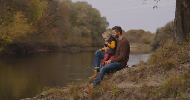 Tôt l'automne dans la forêt, l'homme avec un petit fils marchent par beau temps, l'homme et l'enfant sont assis sur la rive de la rivière — Video