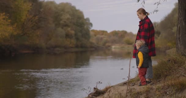 Kleine jongen met zijn moeder staan aan de oever van het schilderachtige bos rivier en genieten van de herfst natuur, reis in het bos in het weekend — Stockvideo