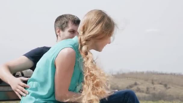 Young couple hugging and sitting on a bench. Hair fluttering in the wind — Stock Video