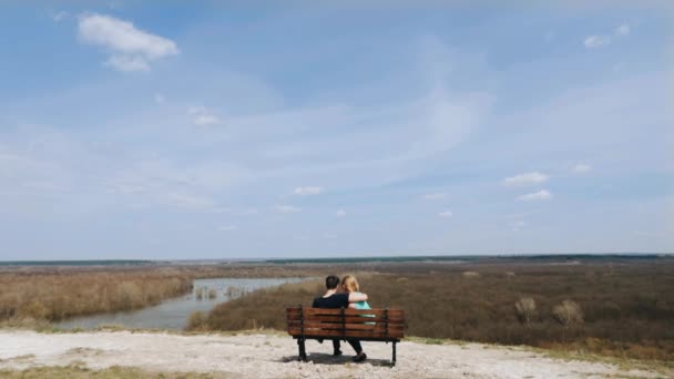 Para zakochanych, siedząc na ławce nad rzeką. Widok z tyłu. — Wideo stockowe