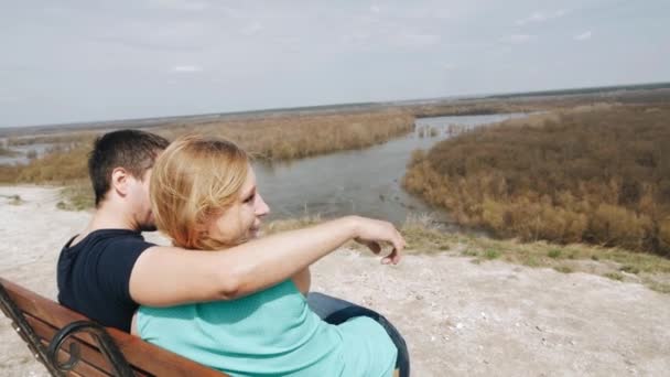 在爱情和幸福的情侣坐在河边的长凳上. — 图库视频影像
