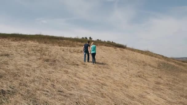 Junges Paar auf einem Hügel, Händchen haltend vor blauem Himmel — Stockvideo