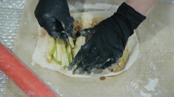 Handschoenenhanden leggen vers fruit voor appelstrudel en bakkerijproducten op het deeg. Noten, rozijnen, vulling — Stockvideo