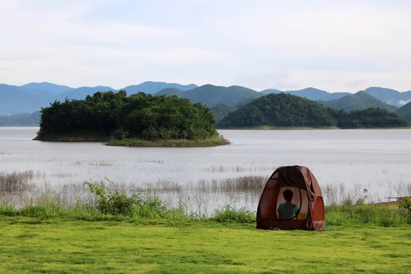 Asian Buddist people are prays meditations in the mesh dome or tents on the lawn with beautiful landscapes of dam water, forests, and mountains in Thailand.