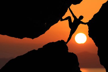 Dağcılık, kırmızı gökyüzü günbatımı arka plan ile kayalar arasında siluet adam