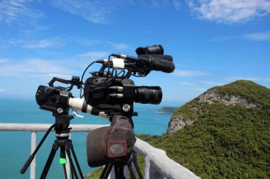 dağın tepesinde bir tripod üzerinde kamera tutan kameraman. Okyanus ve mavi gökyüzü arka plan.