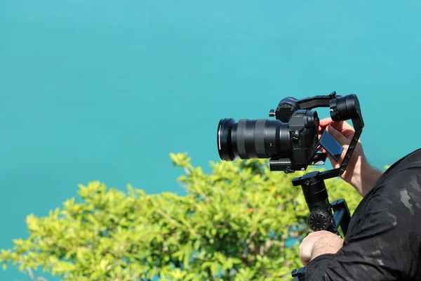 Photographer holding  the Camera Gimbal Stabilizer on top of the mountain. Ocean and blue sky background