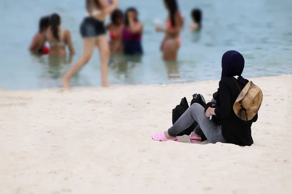 Muslim girl traveler on hijab sitting on the white sand beach