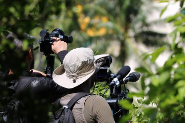 Photographer or videographer holding the video camera on a tripod on top of the mountain. Forest,ocean and blue sky  background.
