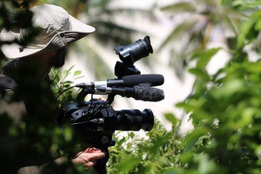 Photographer or videographer holding the video camera on a tripod on top of the mountain. Forest,ocean and blue sky  background.
