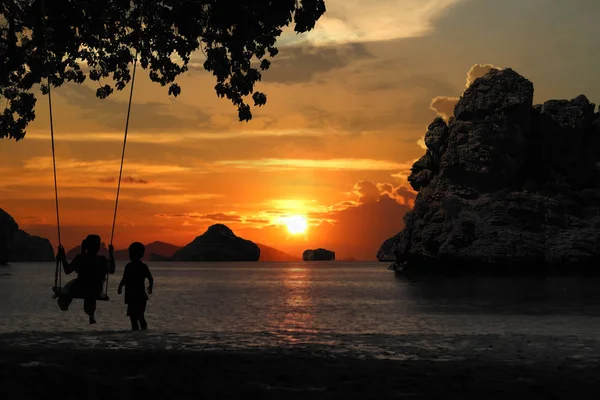 Silhouette of mother and son sitting on cradle or hammock on the beach with red sky sunset background.