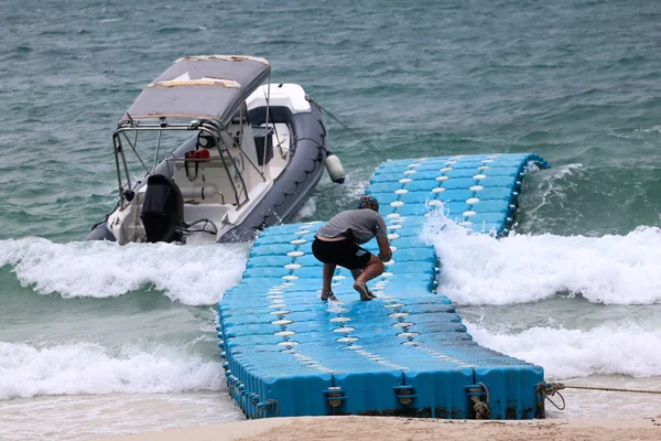 Men walking on the floating pier to the dinghy boat while it is windy and the waves, monsoon