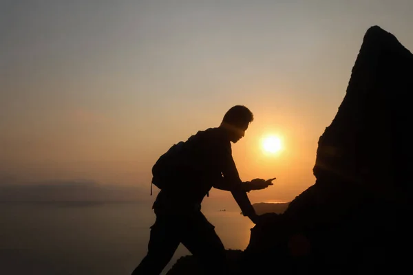 Silhouette of man climbing rock, Photographer on the mountain at sunrise ,Archipelago island in Thailand