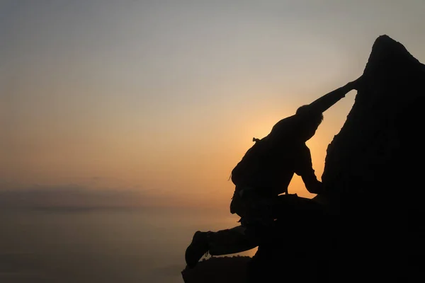 Silhouette of man climbing rock, Photographer on the mountain at sunrise ,Archipelago island in Thailand