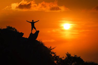 Dağın tepesinde duran adam kırmızı gökyüzü sunse bakıyor