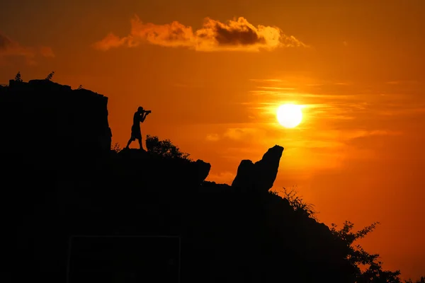 Silhouette of photographer on top of mountain at sunset red sky — Stock Photo, Image