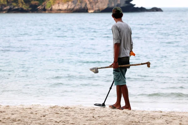 Asyalı erkek bir plajda nesneleri bulmak için metal dedektörü kullanır — Stok fotoğraf