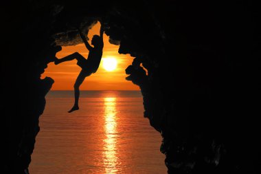 Kırmızı gökyüzü ve gün batımı ile deniz tarafından mağaraya tırmanma adam