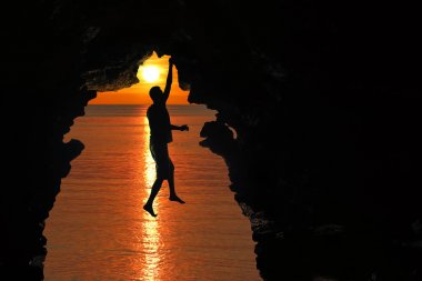 Kırmızı gökyüzü ve gün batımı ile deniz tarafından mağaraya tırmanma adam 