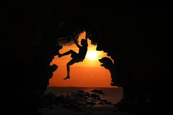 Man climbing in the cave by the sea with red sky and sunset — Stock Photo, Image