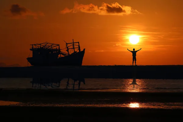 Человек, стоящий рядом со старым разбитым кораблем, брошенным на пляже — стоковое фото