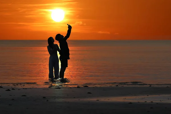 Silueta de parejas asiáticas están disfrutando durante la puesta del sol en el b —  Fotos de Stock