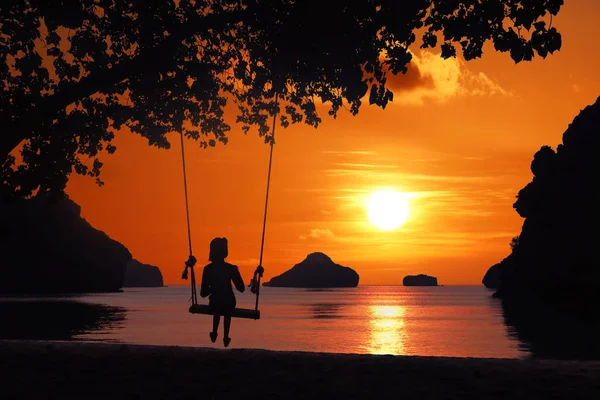 Silhouette of a girl sitting on a swing or cradle on the beach a — Stock Photo, Image