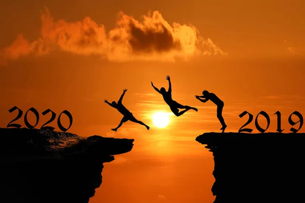 Los hombres son saltados entre un alto acantilado al atardecer de un cielo rojo, Silhouett —  Fotos de Stock